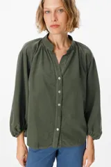Camisa de pana color verde oliva, con cuello mao, cierre frontal de botones y mangas largas abullonadas con puños elásticos.
