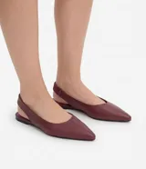 Zapatillas slingback de cuero color bordó, con diseño destalonado, punta fina y costura central en el empeine. Poseen taco plano y tira elástica en el talón.