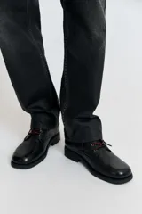 Bota de cuero negro con acabado abatanado, horma cuadrada, cordones rojos en contraste y suela con tacón bloque.