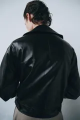 Chaqueta de estilo biker confeccionada en tejido efecto piel con acabado brillante. Presenta cuello con solapas, cierre frontal con cremallera y botones, bolsillos delanteros y bajo ajustable con trabillas y hebilla metálica.