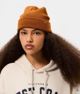 Gorro de punto marrón con borde plegado y pequeña etiqueta cuadrada aplicada en el lateral.