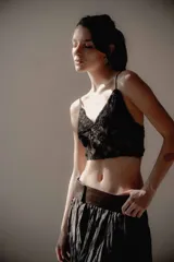 Top corto de encaje negro con breteles finos y detalle de plumas desmontables en el escote. Presenta un diseño ajustado al cuerpo con forro interior.