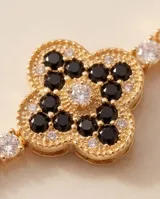 Pulsera de acero con baño dorado, compuesta por una cadena de circonias cúbicas y un dije central en forma de trébol decorado con circonias negras y blancas.