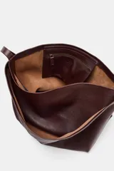 Bolso formato saca color marrón oscuro, confeccionado en piel. Tiene doble compartimento interior, asa de hombro y bolsillo interior con cierre mediante cremallera.