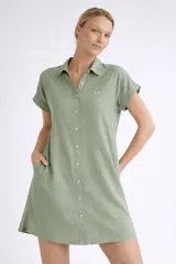 Vestido camisero corto de color verde, confeccionado en viscosa suave y liviana. Presenta cuello clásico, cierre frontal con botones, mangas cortas con dobladillo y bolsillos laterales. Incluye un pequeño detalle bordado de un corazón en el pecho.