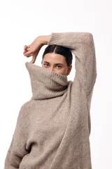 Vestido de punto color beige, de corte holgado y diseño oversized, con cuello alto tipo polera y mangas largas.