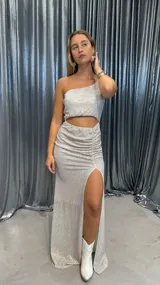 Vestido largo de fiesta con lentejuelas plateadas, corte asimétrico con un solo hombro, abertura en la cintura y tajo en la pierna.