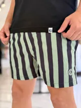 Short de baño con diseño de rayas verticales en tonos verde claro y negro, con parche redondo en el extremo inferior izquierdo.