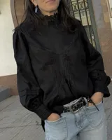 Blusa de lino color salmón con cuello alto, mangas abullonadas y detalle de alforzas en el frente. Presenta terminaciones con puntilla ondulada negra y cierre posterior con botones a la vista.