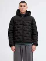 Campera puffer negra con capucha ajustable, cierre frontal y bolsillos laterales. Presenta un diseño acolchado con textura geométrica en el frente, puños con ajuste de velcro y logo sutil en el pecho.