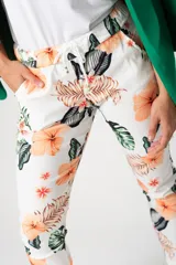 Babucha de corte relajado con estampado tropical de flores y hojas en tonos naranja y verde sobre fondo blanco. Presenta cintura elástica y bolsillos laterales.