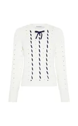Sweater de punto calado en color blanco, con diseño de trenzas y detalles de cintas azul marino entrelazadas verticalmente en el frente. Presenta cuello redondo, mangas largas con puños acanalados y un pequeño lazo decorativo en el escote.