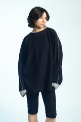 Buzo de felpa negro de corte oversize, con cuello redondo y mangas largas con puños grises doblados hacia afuera. Presenta costuras externas decorativas en tono gris claro a lo largo de las mangas y los hombros.