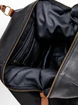 Bolso de viaje grande de cuero marrón con detalles en cuero negro, doble asa de mano y tiras decorativas verticales.