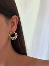 Aro de metal dorado de 2 cm de diámetro, con forma de argolla, adornado con cuentas de vidrio facetadas en tonos blanco opaco y dorado/ámbar.