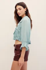 Camisa crop de viscosa color verde menta, con escote en V pronunciado, volados en el cuello y el frente, y mangas tres cuartos con puños elastizados.