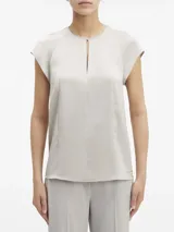 Blusa de satén color gris claro, con cuello redondo y abertura en forma de gota. Tiene mangas cortas con costuras en los hombros y cierre con broche en la espalda.