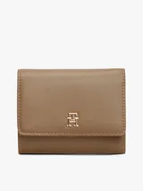 Billetera trifold de Tommy Hilfiger en color marrón, confeccionada en poliuretano con textura granulada. Presenta un diseño plegable con solapa frontal y el logo metálico TH en tono dorado en el centro.