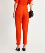Pantalón zanahoria color naranja, marca Cortelle, con pliegues, bolsillos laterales y traseros, detalle de botón en los bajos y cierre en la cintura por botón.