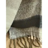 Bufanda rectangular de tejido grueso con diseño de cuadros en tonos azul, naranja, gris y beige, terminada con flecos en los extremos.