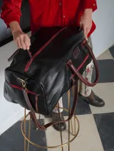 Bolso de viaje tipo weekender de cuero color tostado con asas y detalles en marrón oscuro, herrajes metálicos y bolsillo frontal con cierre.