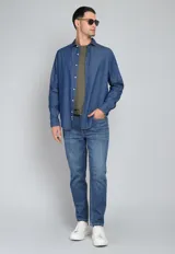 Camisa de jean azul con botones blancos, mangas largas con puños doblados y corte clásico.