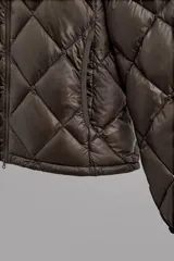 Campera puffer verde oliva acolchada con diseño de rombos, capucha y cierre frontal con cremallera. Incluye bolsillos laterales con cierre. Relleno de plumón y plumas.