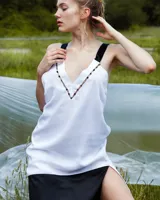 Vestido corto blanco de gasa y seda fina, con escote pronunciado y apliques de perlas de vidrio. Espalda abierta con tirantes cruzados anchos y caída asimétrica.