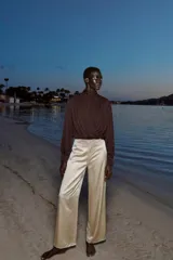 Blusa corta marrón de tejido fluido y semitransparente, con cuello subido, diseño cruzado drapeado en el frente y mangas largas abullonadas con puños ajustados.