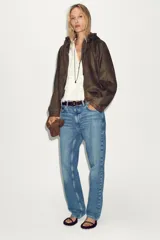 Chaqueta bomber de efecto ante en color marrón, con capucha ajustable mediante cordones, cierre frontal con cremallera, bolsillos laterales y bajo con elástico interior.