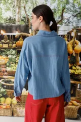 Blusa celeste de denim con cuello polo, manga larga y botones marrones.