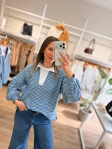 Buzo tipo chomba de corte oversize con diseño a rayas horizontales celestes y blancas. Presenta cuello camisero blanco y un bordado en la espalda con la inscripción República Oriental del Uruguay.