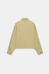 Cazadora bomber de color beige con cuello subido, manga larga y bolsillos delanteros. Cuenta con cierre frontal de cremallera metálica y cordón ajustable en el dobladillo.