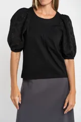 Remera negra de algodón con mangas globo confeccionadas en tela broderie con diseño floral calado. Presenta cuello redondo y costura central vertical en el frente.