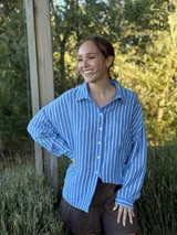 Camisa celeste con rayas verticales blancas, de manga larga, cuello camisero y cierre frontal con botones.