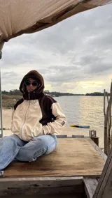 Campera de gabardina con diseño bicolor en tonos crudo y chocolate, con capucha forrada en polar. Presenta cierre frontal, mangas largas con puños elásticos y un parche distintivo en la manga.