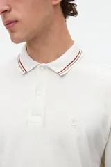 Remera polo manga corta color blanco, confeccionada en tela piqué de algodón lavado con textura extra suave. Cuenta con media cartera de botones, cuello y puños acanalados con diseño de líneas a contratono, y bordado sutil de la marca en el pecho. Calce clásico.