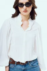 Camisa blanca de manga larga abullonada, con cuello alto y volados delicados en el borde.
