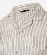 Camisa de manga corta con cuello inglés y abotonadura frontal. Diseño con encaje bicolor texturizado en tonos beige y blanco. Corte regular.