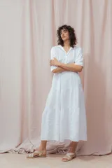 Vestido midi blanco de lino, con cuello camisero, botonera frontal y mangas 3/4. Presenta un calce relajado con frunces en la cintura.