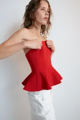 Top rojo sin tirantes, de escote recto y hombros descubiertos, con diseño ajustado en el torso y bajo acabado con peplum. Cierre lateral con cremallera oculta.