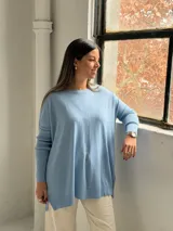 Sweater de punto color celeste, con cuello redondo, corte holgado y mangas largas con puños acanalados. Presenta un detalle de costura vertical central en el frente.
