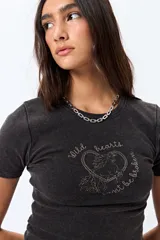 Remera blanca de corte ajustado con cuello redondo y mangas cortas. Presenta una estampa frontal en color marrón con el texto 'Wild hearts can't be broken' y un diseño de caballo dentro de un corazón.