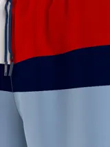 Short de baño celeste con cintura elástica, cordón de ajuste y diseño color block con los colores blanco, azul marino y rojo.