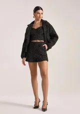 Chaqueta de tweed color negro con hilos metalizados, diseño estructurado, cuello solapa y cierre frontal con cremallera.