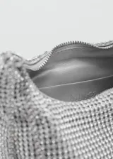 Bolso de mano tipo baguette con diseño estructurado, recubierto completamente por cristales facetados sobre una base de aluminio. Cuenta con doble asa de cadena metálica, cierre superior de cremallera y forro interior de poliéster.