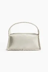 Cartera pequeña de color blanco hueso, con diseño rectangular y detalles entrelazados en los bordes y en el asa superior. Cuenta con cierre superior.