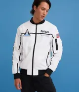 Campera tipo bomber blanca con detalles en negro, inspirada en uniformes espaciales de la NASA. Presenta parches con el logo de la NASA, la bandera de EE. UU. y texto en la manga que dice "Kennedy Space Center".