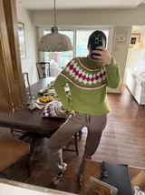 Sweater tejido a mano en mohair, de color marrón con diseño de canesú estampado con corazones fucsias y detalles geométricos en tonos beige y rosado. Presenta cuello redondo y mangas largas.
