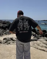 Remera de manga corta negra con diseño gráfico en la espalda que muestra dos gatos animados con cuchillos y el texto 'Kaboa Industries'.